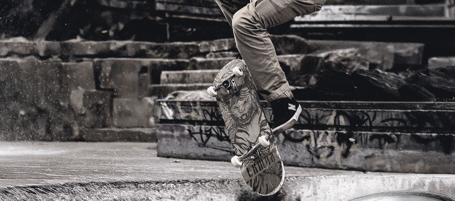 A skateboarder catches air mid-trick, kickflip, on a gritty, graffiti-covered stair set, showcasing the bold LXMNA skateboard deck. Featuring a fierce tiger graphic and built for street performance, Laksamana boards are made for skaters who ride hard and stand out. Perfect for urban skate sessions and fearless style.